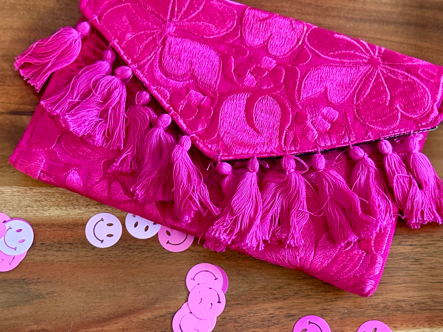 Pink clutch bag with tassels on a wooden surface