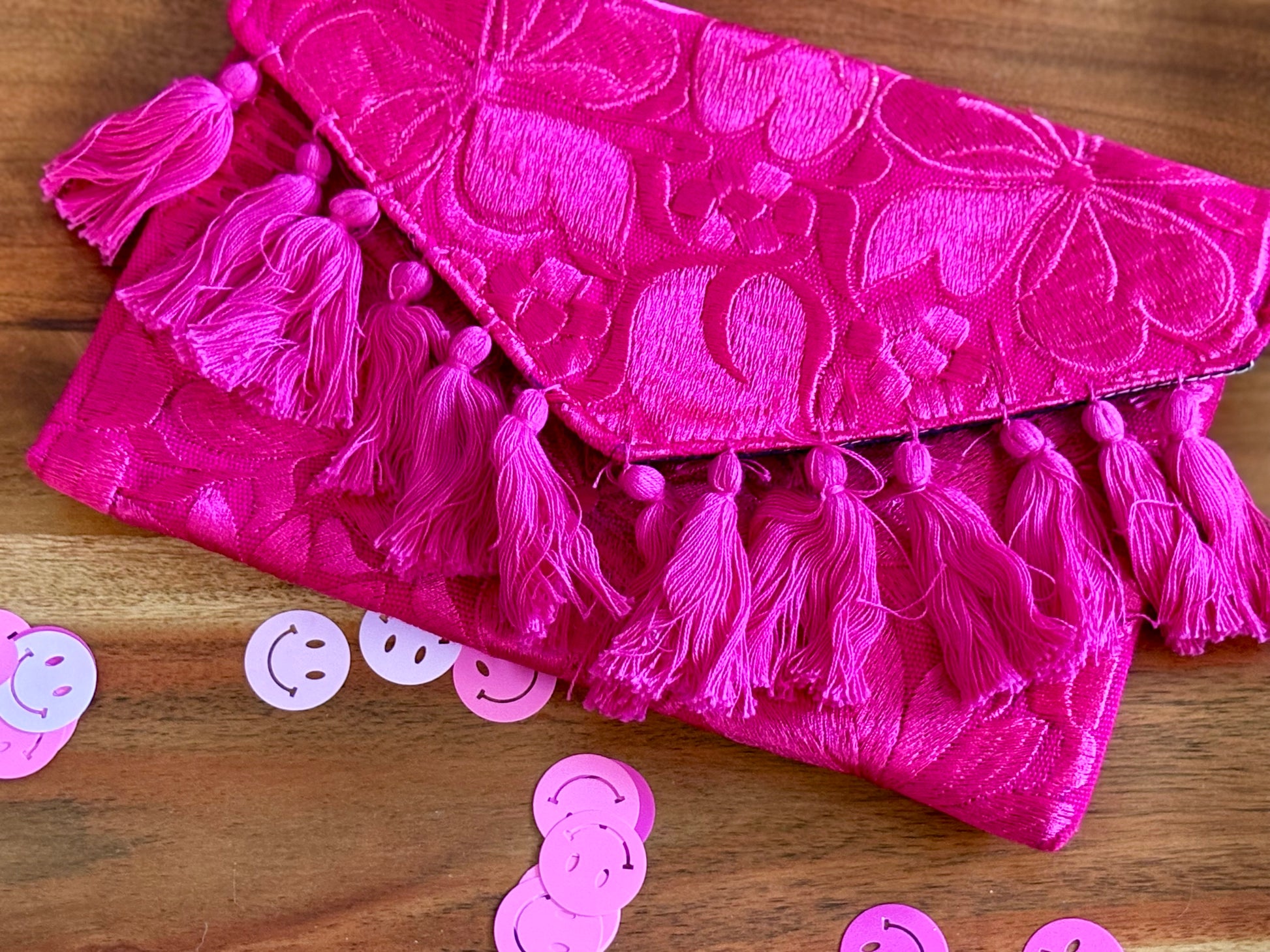 Pink clutch bag with tassels on a wooden surface