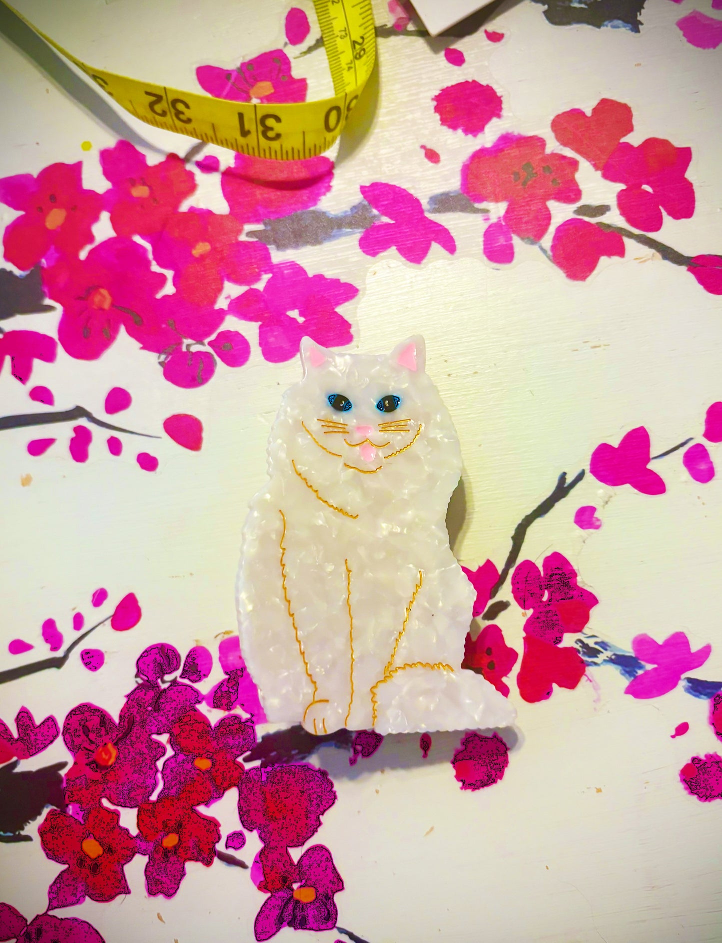 White cat-shaped plush toy on a floral background with a measuring tape.